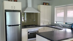 A modern kitchen with white cabinets, a stainless steel refrigerator, a gas stove, and a built-in oven.