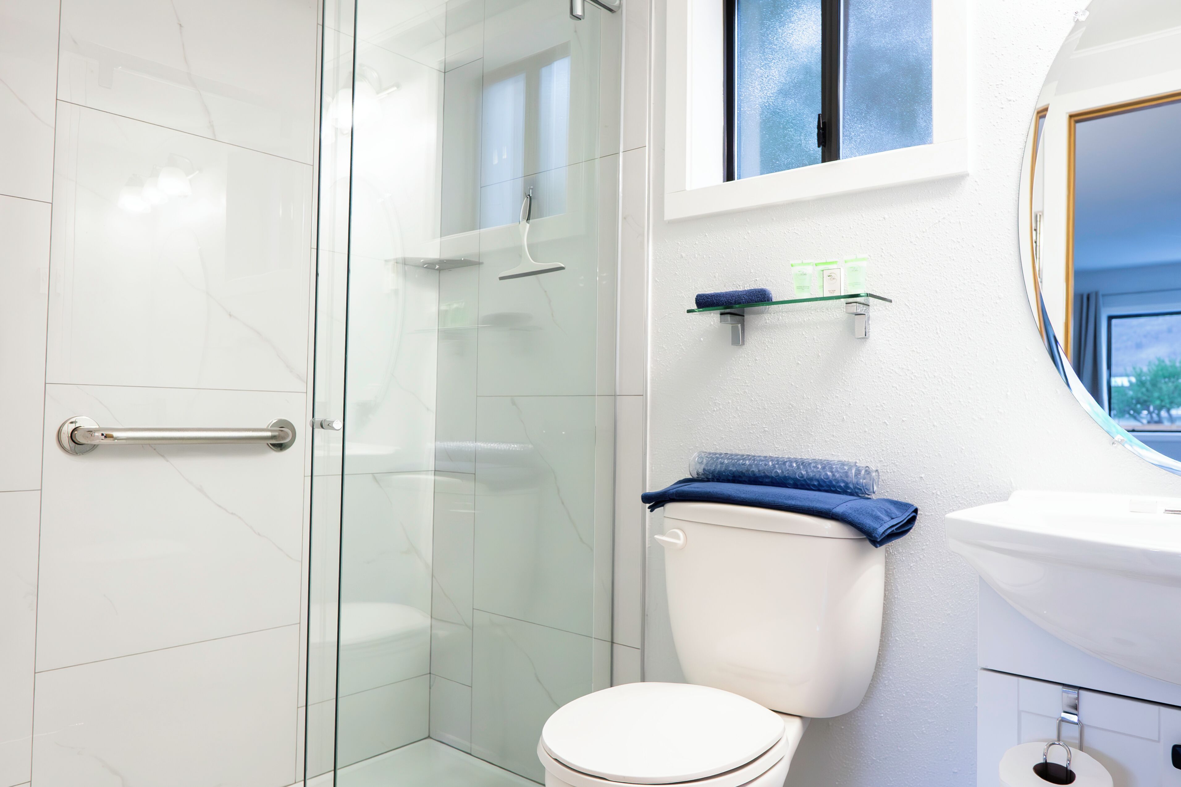 A modern bathroom with a glass shower enclosure, a white toilet, and a sink with a window above it.