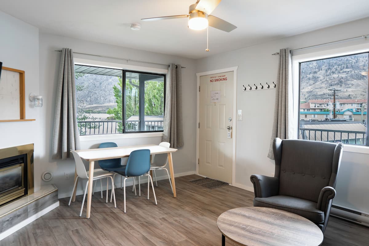 Una habitación con una mesa de comedor, sillas, chimenea, ventilador de techo y vistas a un paisaje montañoso a través de grandes ventanales.
