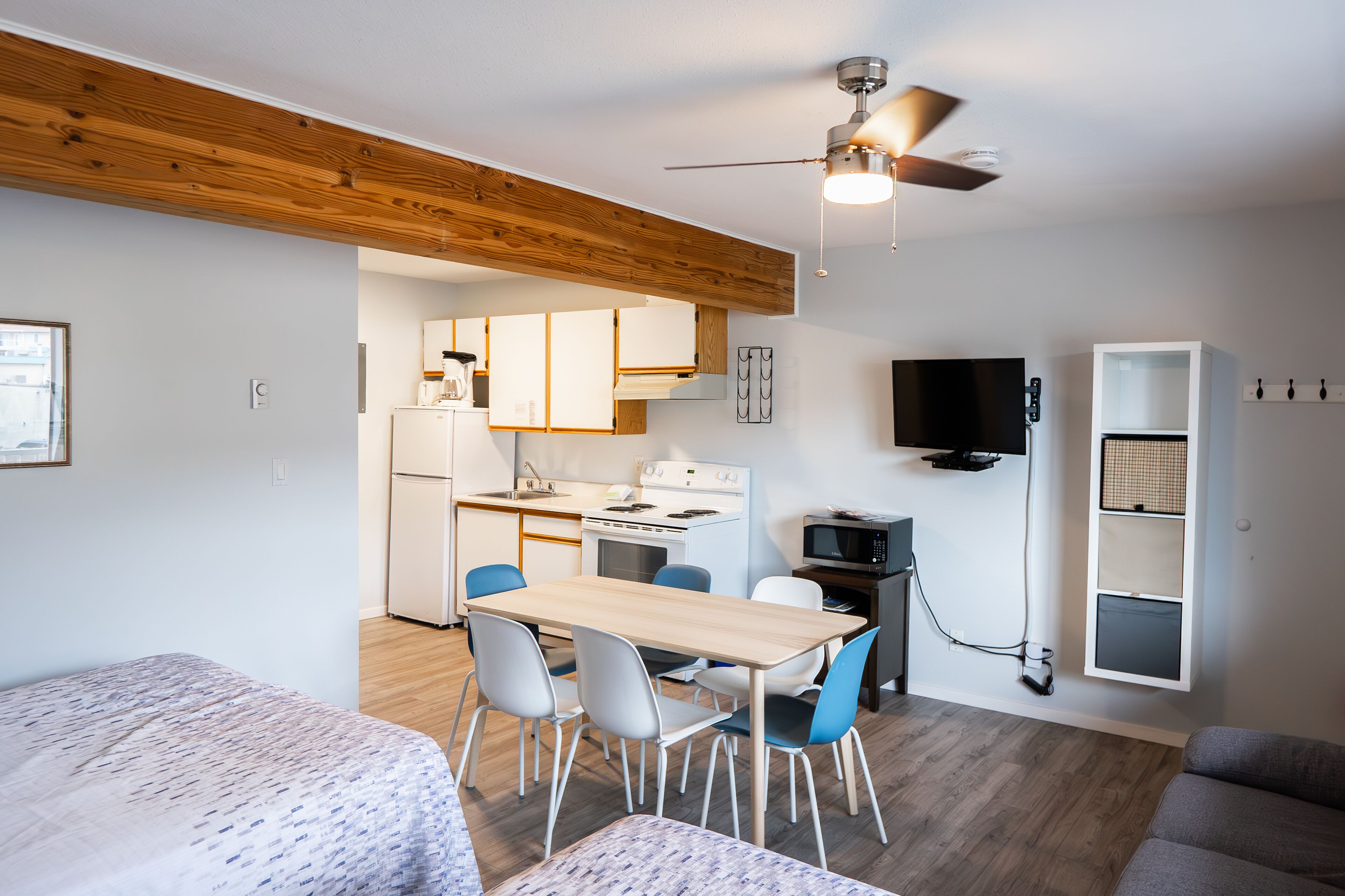 Un espace de vie compact comprenant un coin cuisine, un coin repas et un téléviseur fixé au mur.