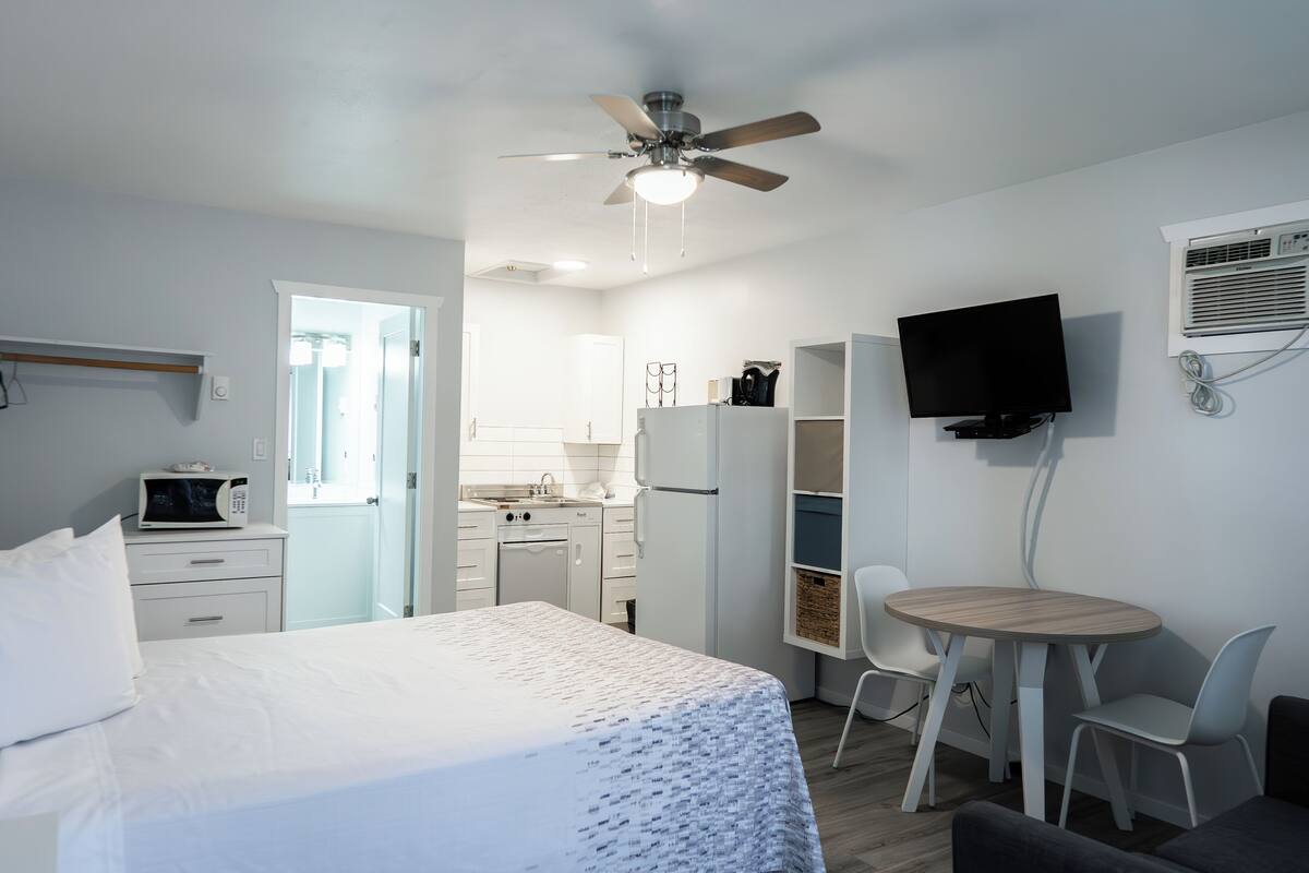 Una habitación de hotel con cama, escritorio, silla, televisor y kitchenette.
