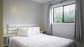 Un dormitorio con cama, mesitas de noche, ventilador de techo y ventana con cortinas.