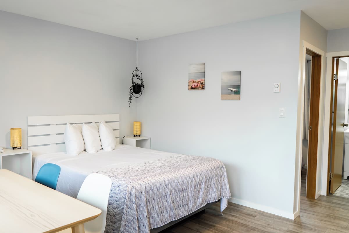 Un dormitorio ordenado con una cama, mesitas de noche, un escritorio y una silla.