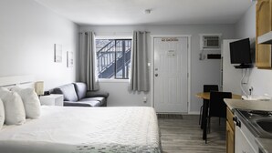 Una habitación de hotel con cama, escritorio, silla, televisor y zona de cocina.