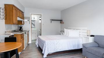 Una habitación de hotel pequeña con cama, un sofá gris, una mesa de comedor de madera y una kitchenette.
