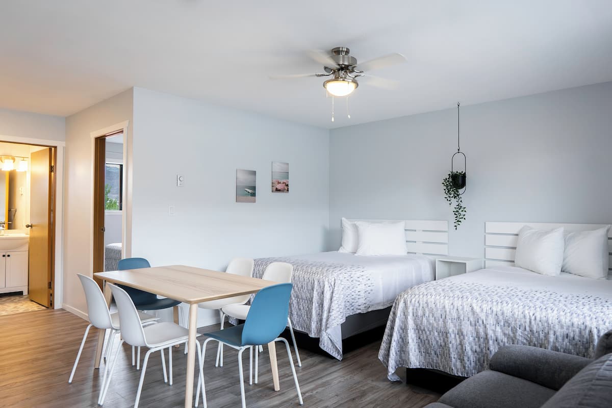 Una habitación de hotel moderna con una mesa de comedor de madera, dos camas individuales, un sofá y un ventilador de techo.