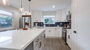 Moderni keittiö, jossa on valkoiset kaapit, suuri keittiösaareke ja riippuvalaisimet.