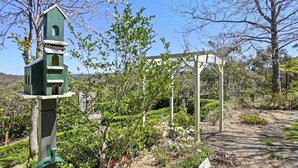 A garden with a birdhouse and a pergola structure. - Romantic Cottage in the Blue Mountains with Valley Views (Hazelbrook)