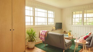 A living room with a sofa, a small table, a TV, and a potted plant. - Romantic Cottage in the Blue Mountains with Valley Views (Hazelbrook)