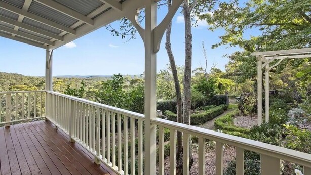 A covered outdoor area with a wooden deck and white railings, surrounded by lush greenery and trees. - Romantic Cottage in the Blue Mountains with Valley Views (Hazelbrook)