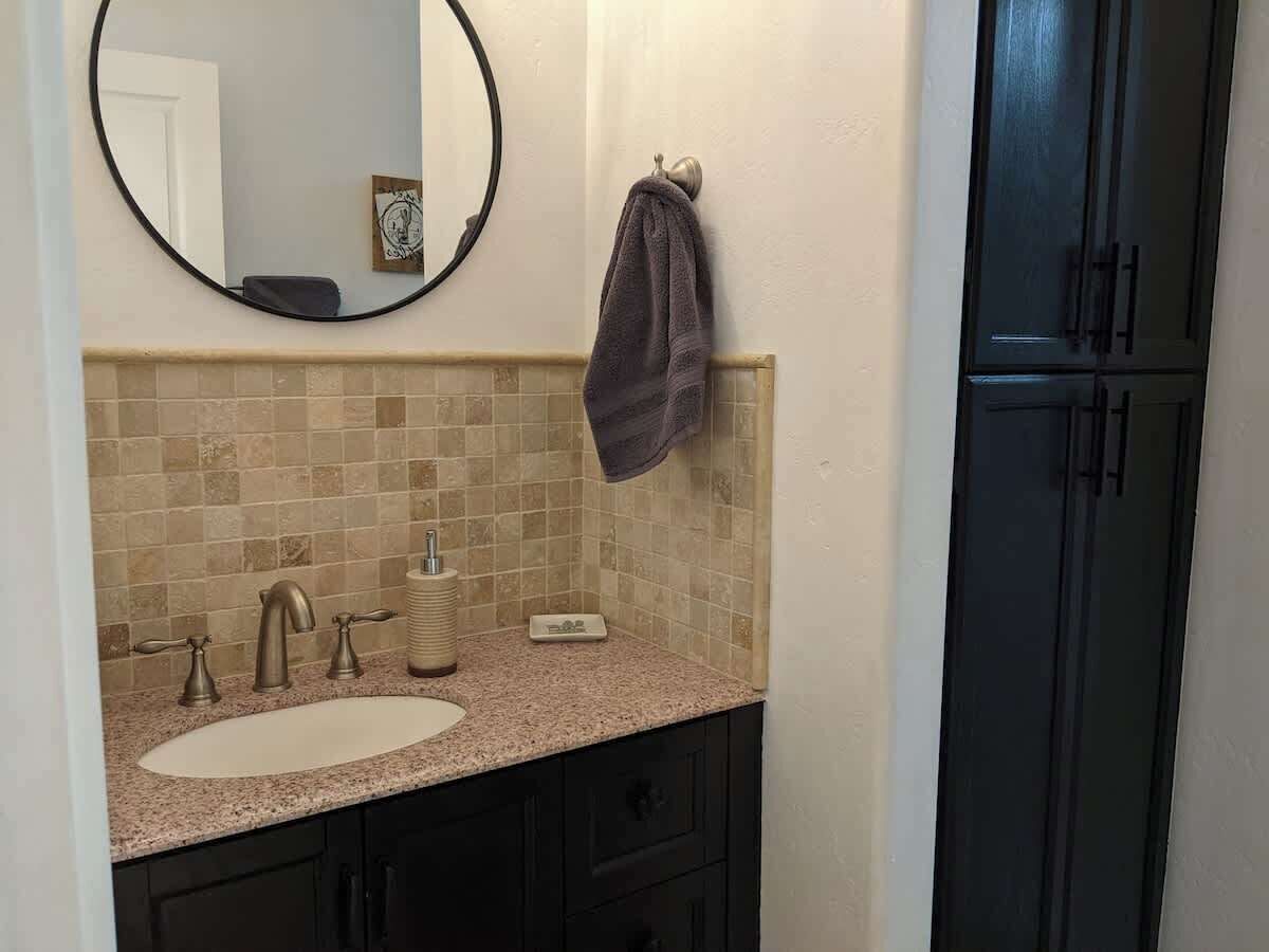 Une salle de bain avec un lavabo, un miroir, un porte-serviettes et des meubles de rangement de couleur sombre.