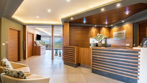 A hotel reception area with a wooden reception desk, a TV, and a view of the mountains.
