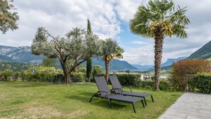 A garden with two black lounge chairs, a paved walkway, and a view of mountains in the background.