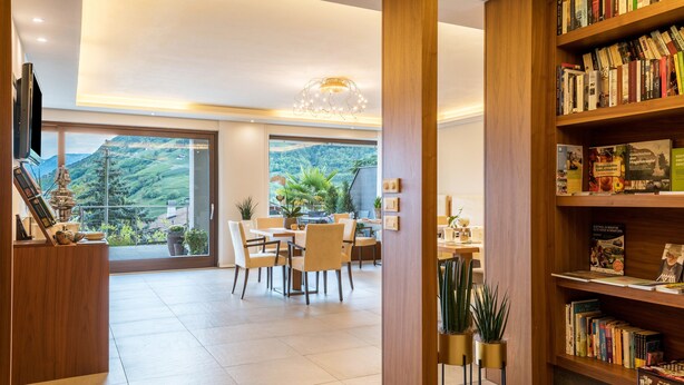 A spacious room with a dining area, a bookshelf, and a large window offering a view of a mountainous landscape.
