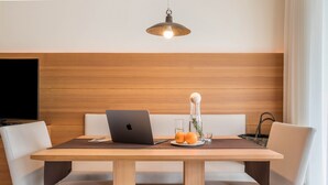 Een moderne eetruimte met een houten tafel, witte stoelen met kussens, een laptop, een glazen vaas met bloemen en een schaal fruit.