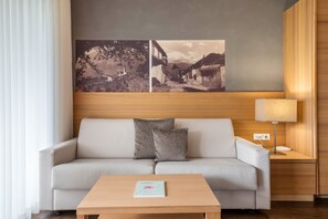 Een moderne hotelkamer met een bank, een bijzettafeltje, een lamp en twee foto’s aan de muur.