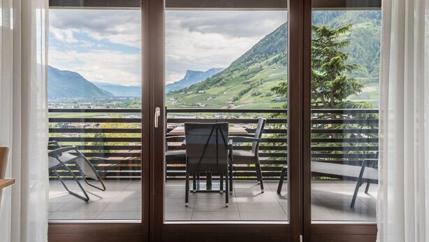 Een balkon met een tafel en stoelen, met uitzicht op een bergachtig landschap.