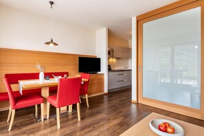 Une cuisine moderne dotée d’un téléviseur à écran plat, de meubles en bois et d’un coin repas avec des chaises rouges et une table blanche.