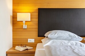 Ein ordentlich bezogenes Bett mit weißer Bettwäsche, ein Nachttisch mit Lampe und ein Buch.