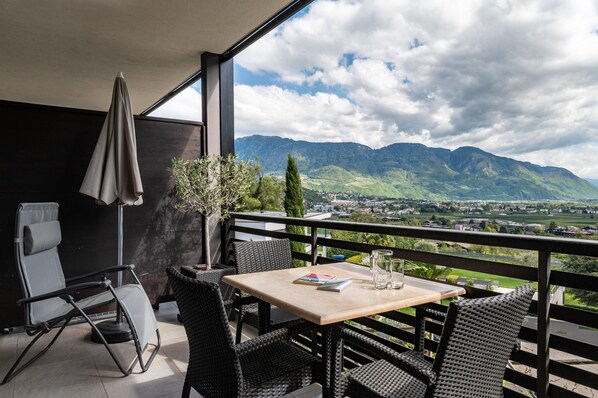 Un balcon avec une table, des chaises, une chaise pliante et une vue sur les montagnes.
