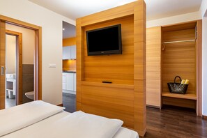 Une chambre d’hôtel moderne avec un lit, un téléviseur fixé au mur en bois, une armoire et une salle de bain visible à travers une porte ouverte.