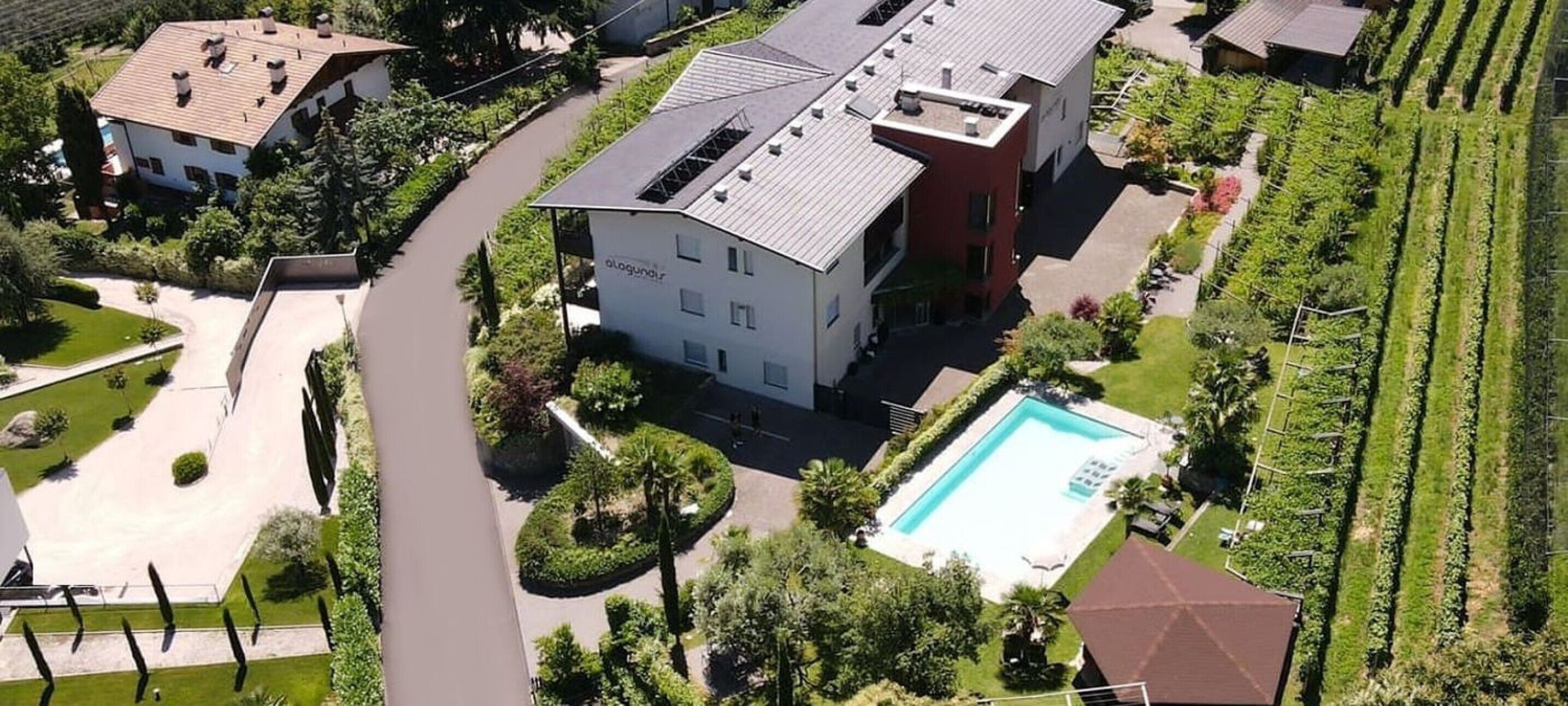 Un edificio de varios pisos con piscina, rodeado de jardines cuidados y un viñedo.