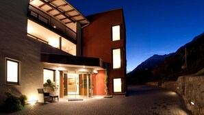 A modern building with a glass entrance, outdoor seating, and a mountain backdrop. - Apartment 'Alagundis  Aurum II' with Mountain View, Shared Pool and Wi-Fi (Lagundo)