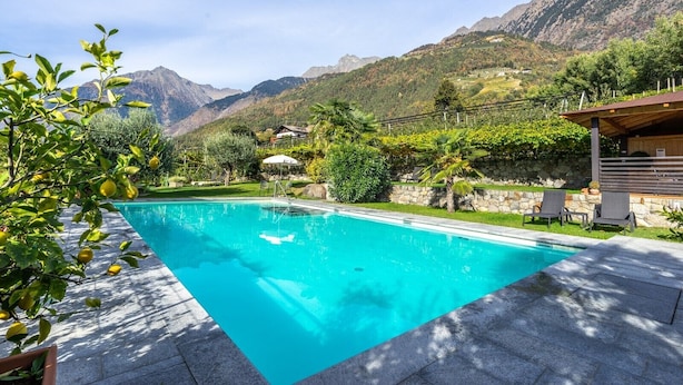 A swimming pool with a mountain backdrop, surrounded by greenery and a stone wall. - Apartment 'Alagundis  Aurum II' with Mountain View, Shared Pool and Wi-Fi (Lagundo)