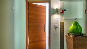 A hallway with a wooden door, a wall-mounted light, a fire alarm, and a green plant in a basket. - Apartment 'Alagundis  Aurum II' with Mountain View, Shared Pool and Wi-Fi (Lagundo)