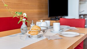 A breakfast setting with a bowl of pastries, a vase with flowers, a coffee pot, and a television in the background. - Apartment 'Alagundis  Argentum Familia' with Mountain View, Shared Pool and Wi-Fi (Lagundo)