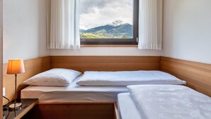 A hotel room with two beds, a window with curtains, a bedside lamp, and a view of mountains. - Apartment 'Alagundis  Argentum Familia' with Mountain View, Shared Pool and Wi-Fi (Lagundo)
