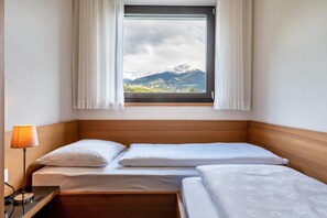 Une chambre d’hôtel avec deux lits, une fenêtre avec des rideaux, une lampe de chevet et une vue sur les montagnes.