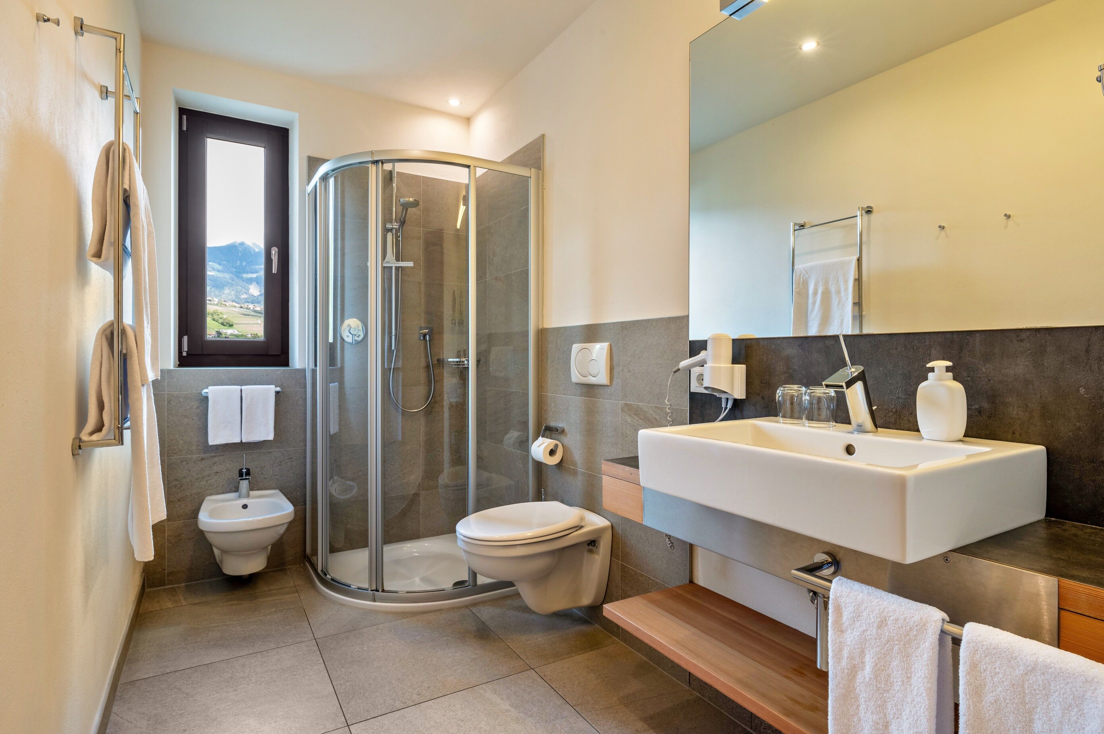 Ein modernes Badezimmer mit Duschkabine aus Glas, einem Bidet, einer Toilette und einem großzügigen Waschbecken mit Spiegel darüber.