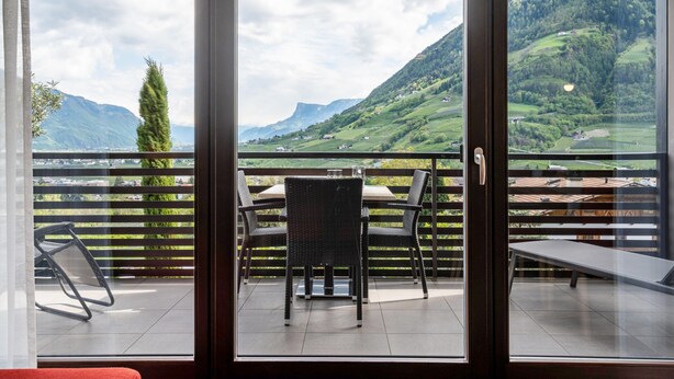 A balcony with a table and chairs, a bench, and a view of a mountainous landscape. - Apartment 'Alagundis  Argentum Familia' with Mountain View, Shared Pool and Wi-Fi (Lagundo)