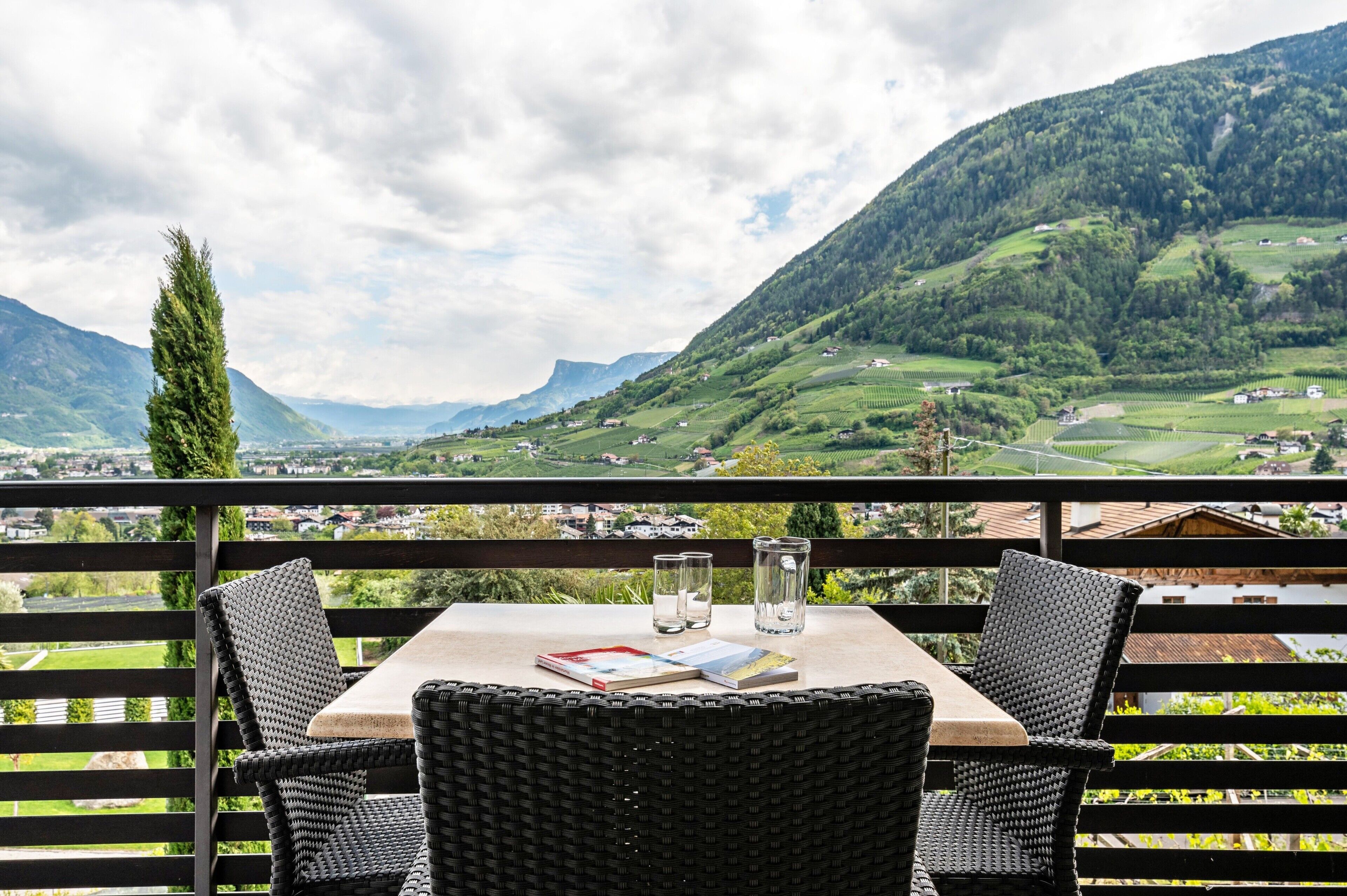Eine Terrasse mit Korbstühlen, einem Tisch und Blick auf eine gebirgige Landschaft.