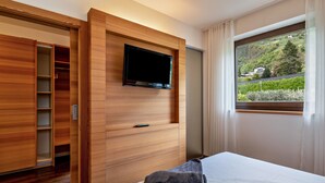 Quarto de hotel com cama, televisão na parede, guarda-roupa e janela com vista para o verde.