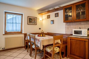 Une cuisine avec des meubles de rangement en bois, une table à manger avec des chaises, une fenêtre avec des rideaux et un four à micro-ondes.