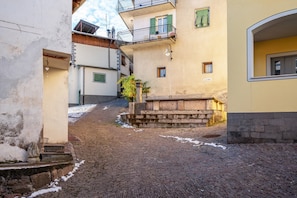 A cobblestone street with buildings on either side, a staircase, and a small tree.