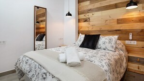 Ein Schlafzimmer mit einem hölzernen Kopfteil, einem Bett mit floralem Bettbezug, einem Spiegel und zwei Pendelleuchten.