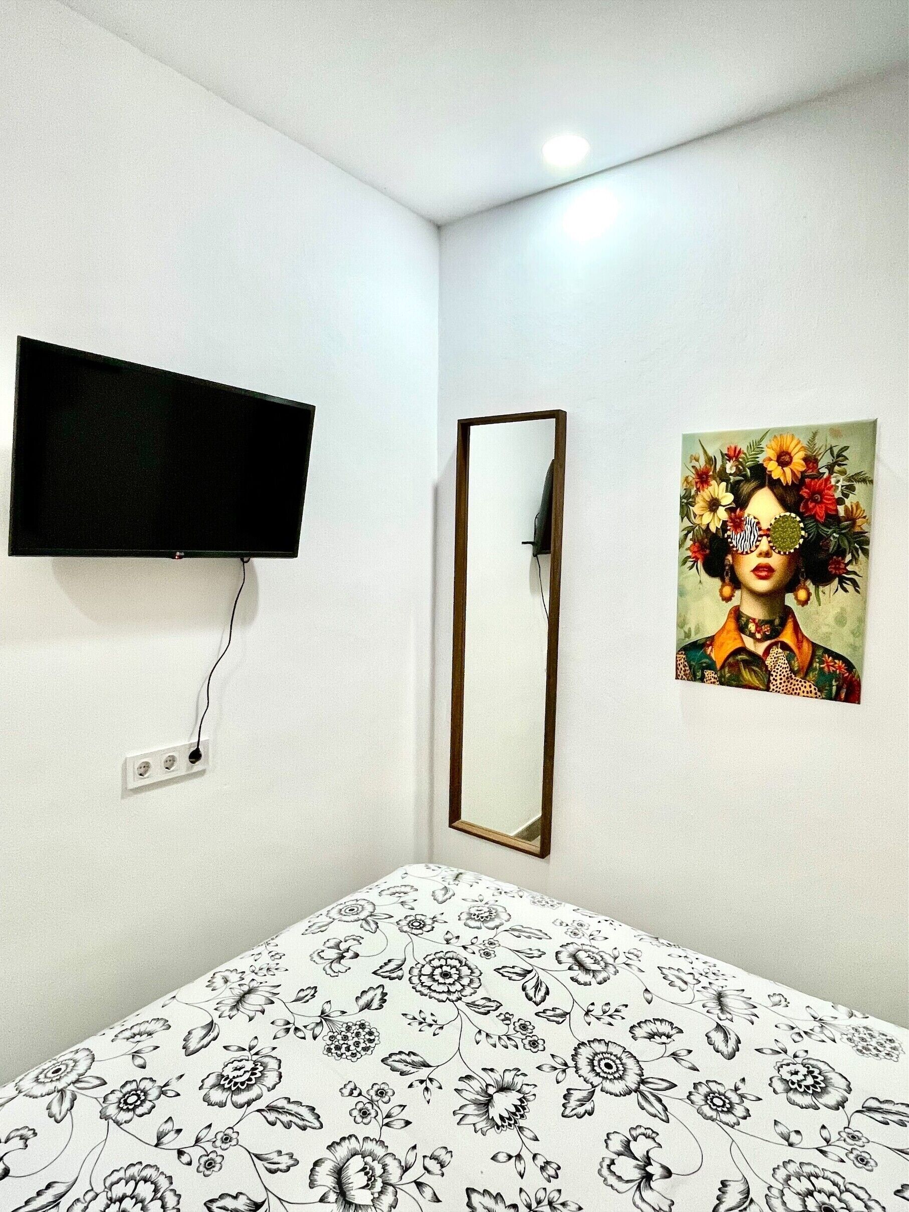 Een kamer met een bed, een aan de muur bevestigde televisie, een spiegel en een bloemschilderij.
