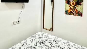Een kamer met een bed, een aan de muur bevestigde televisie, een spiegel en een bloemschilderij.
