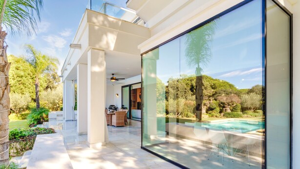 Une maison moderne dotée d’une grande baie vitrée, d’une piscine et d’un espace patio.
