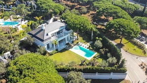 Une grande maison avec une piscine, entourée d’une végétation luxuriante et d’arbres.