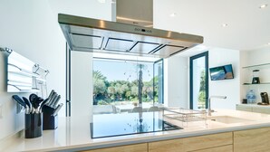 Une cuisine moderne dotée d’un grand îlot central, d’une hotte en acier inoxydable et offrant une vue sur l’extérieur.