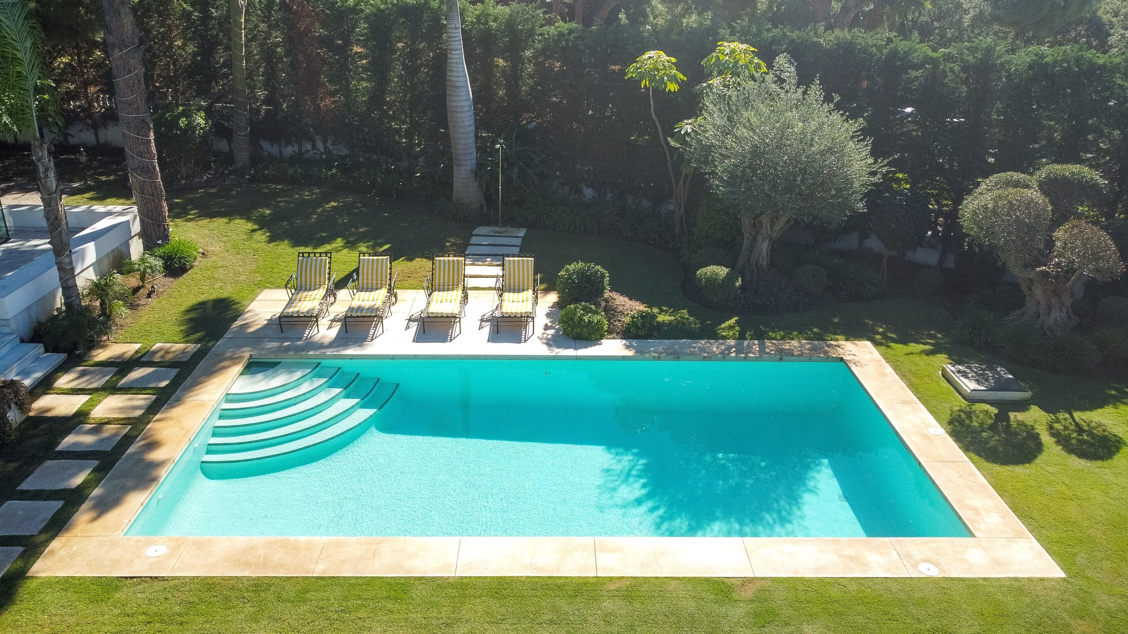 A rectangular swimming pool with a clear blue water surface, surrounded by a well-maintained lawn and several lounge chairs.