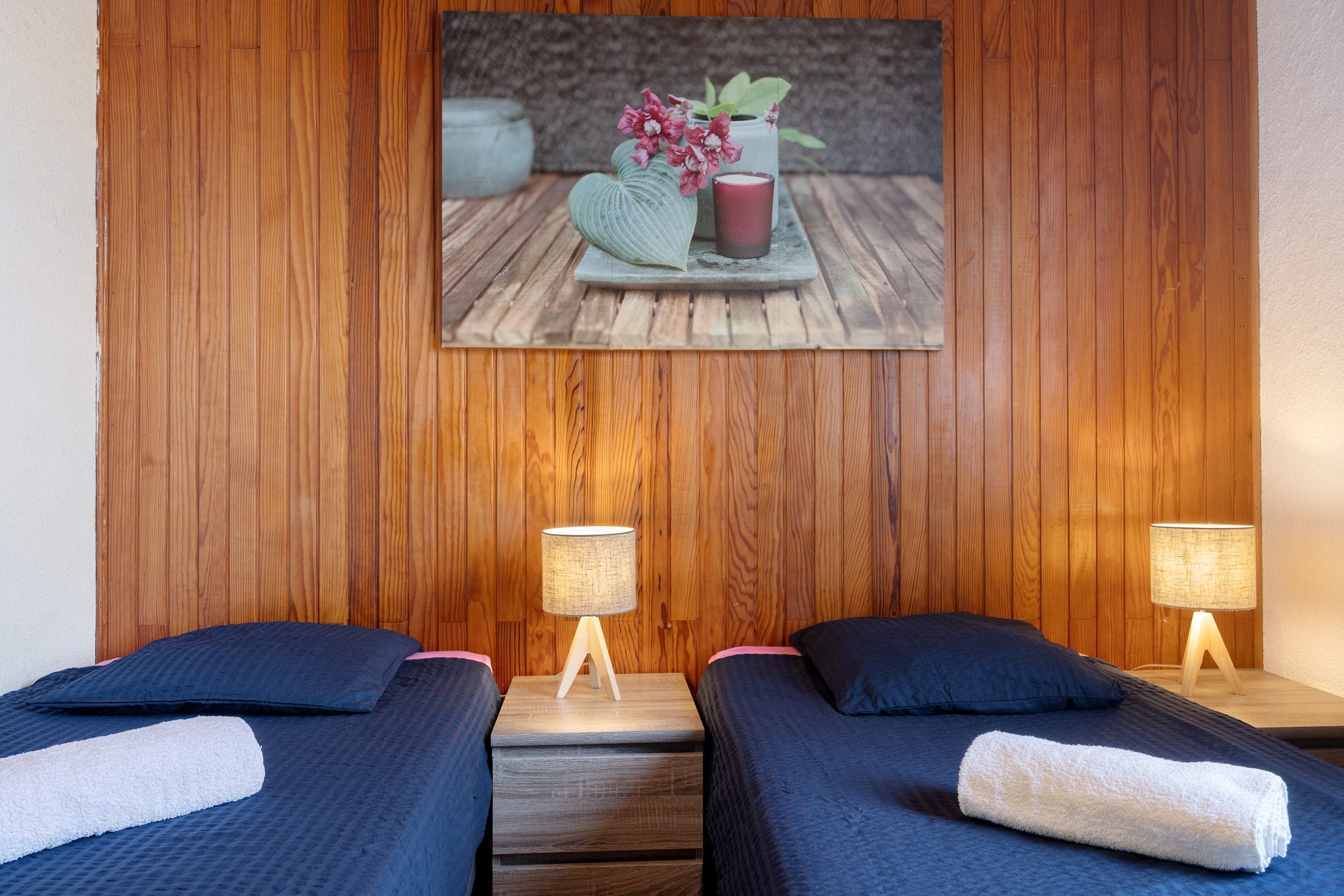 Une chambre d’hôtel avec deux lits, des têtes de lit en bois, une petite table sur laquelle est posé un vase de fleurs, et deux lampes de chevet.