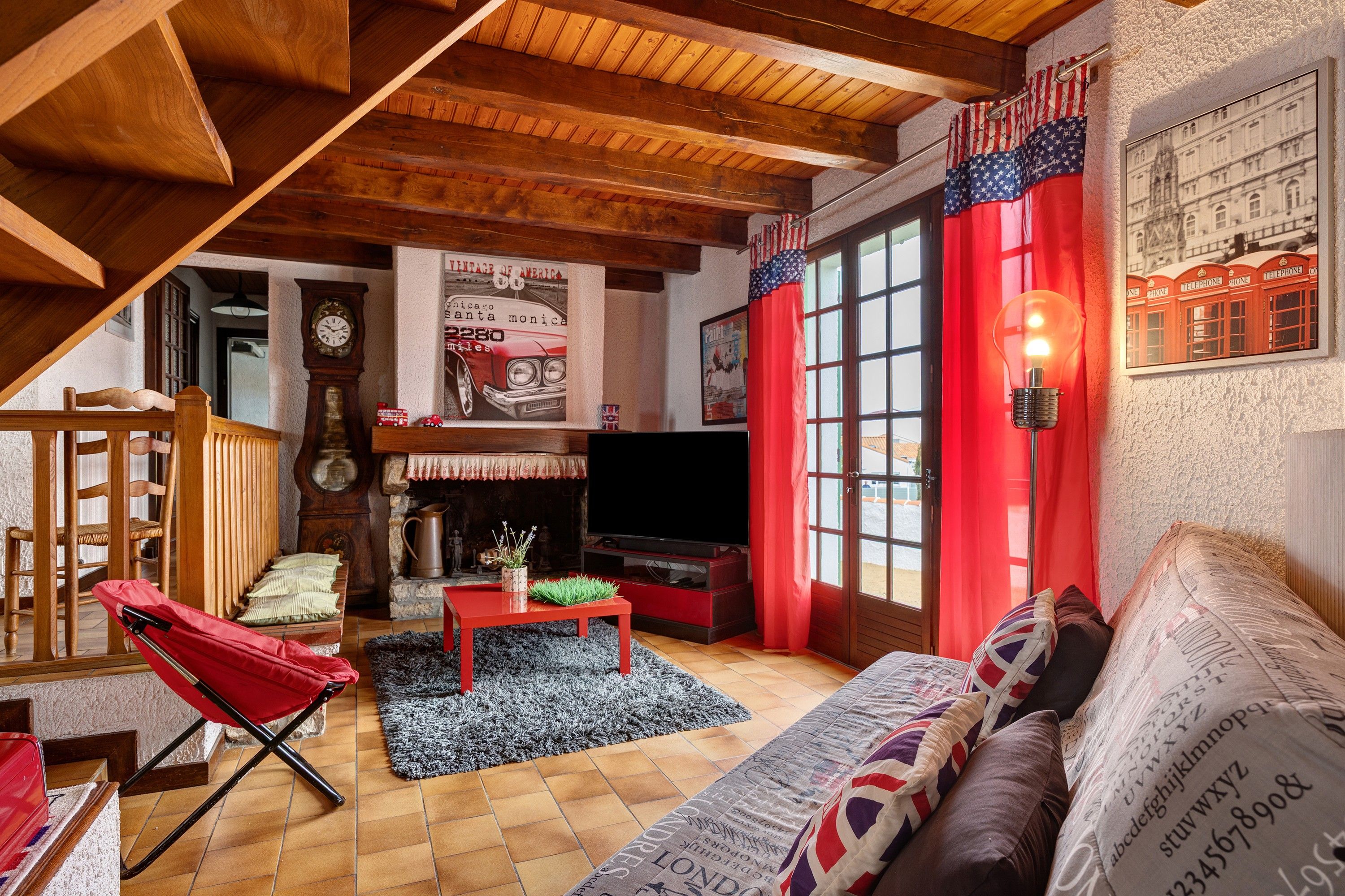A cozy living room with a fireplace, a red sofa, a wooden ceiling, and a vintage poster.