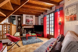 Een gezellige woonkamer met een open haard, een rode bank, een houten plafond en een poster uit vervlogen tijden.