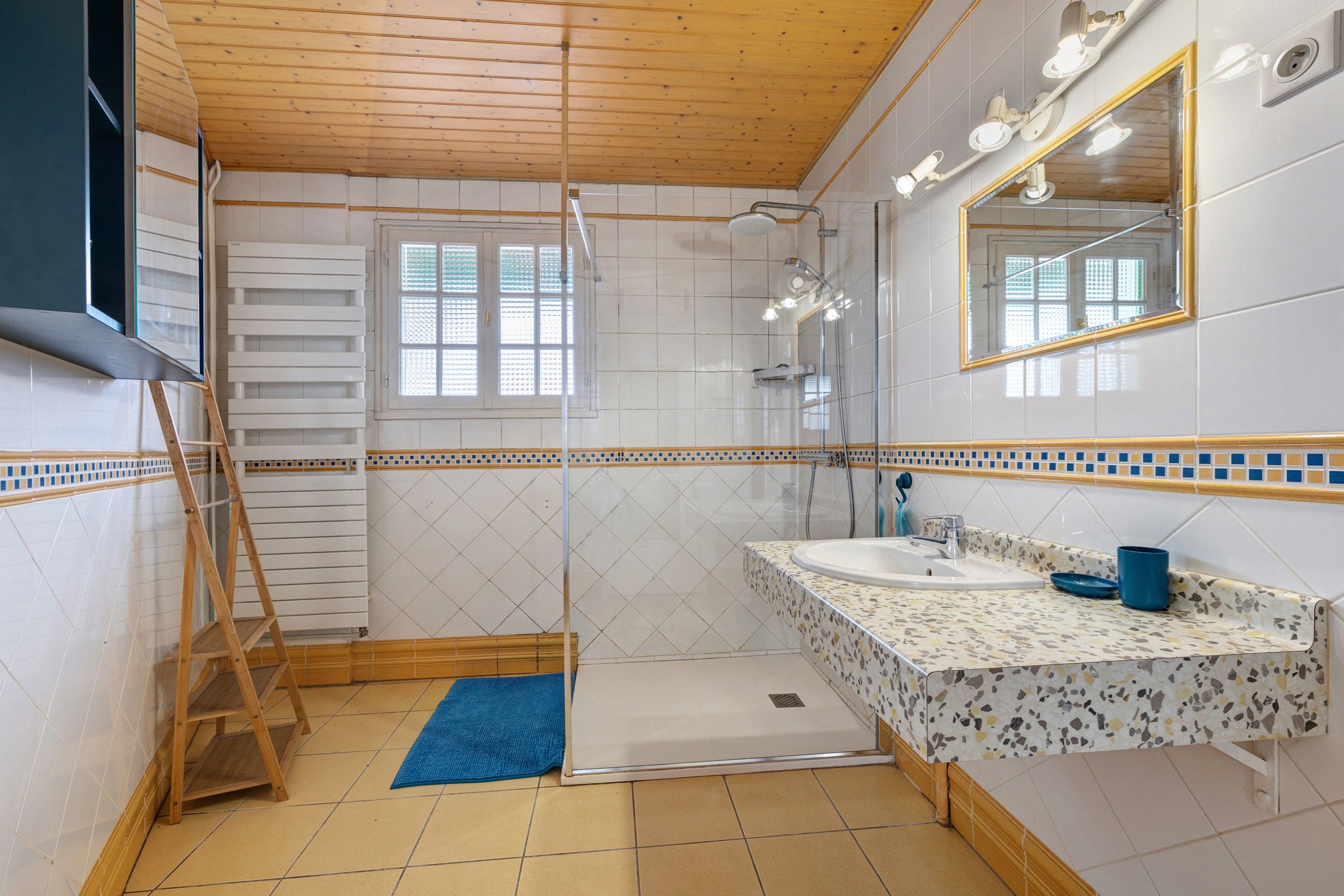 Een badkamer met een douche, een wastafel met spiegel en een houten trap.
