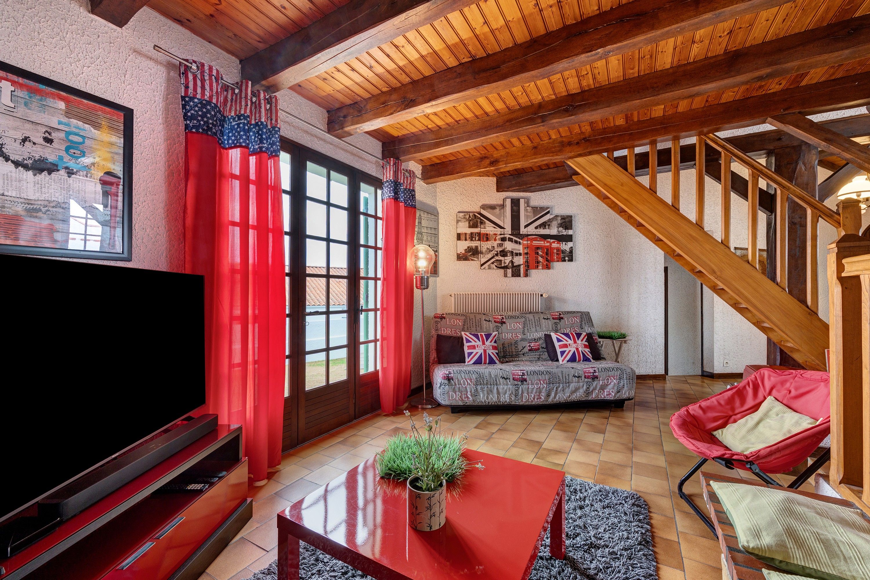 A living room with a TV, red curtains, a sofa, and a staircase.